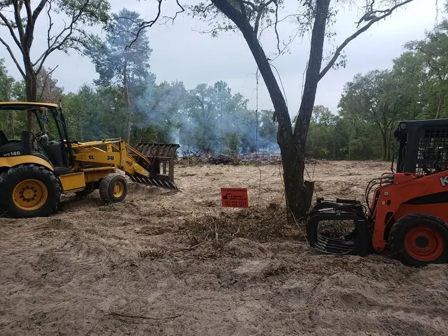 Skid steer with a grapple attachment removing brush on a cleared lot in Ocala